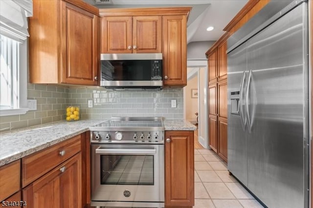 kitchen featuring stainless steel appliances, brown cabinetry, backsplash, and light tile patterned floors