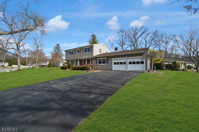 colonial house with aphalt driveway, a garage, a chimney, and a front lawn