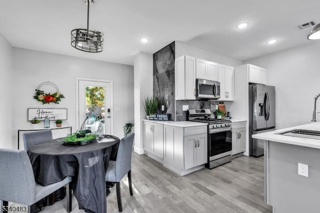 kitchen with stainless steel appliances, a sink, visible vents, light wood-style floors, and light countertops