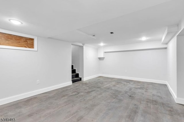 finished below grade area featuring stairs, baseboards, and wood finished floors