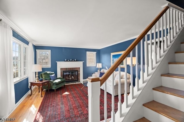 staircase featuring crown molding, a fireplace, baseboards, and wood finished floors