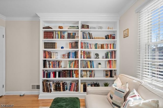 living area with wood finished floors, visible vents, built in features, baseboards, and ornamental molding