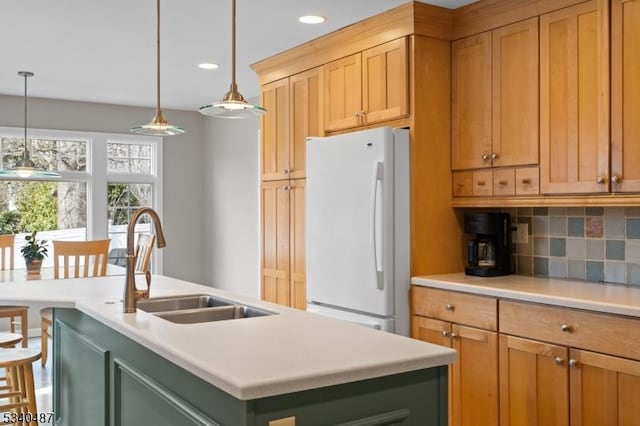 kitchen featuring light countertops, decorative backsplash, freestanding refrigerator, a sink, and an island with sink