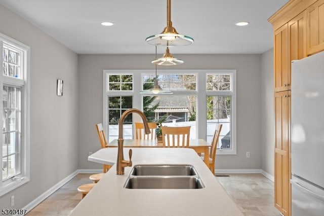 kitchen featuring white fridge, decorative light fixtures, light countertops, light brown cabinetry, and a sink