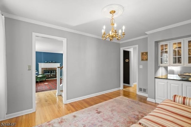 living room with a brick fireplace, baseboards, visible vents, crown molding, and light wood-style floors