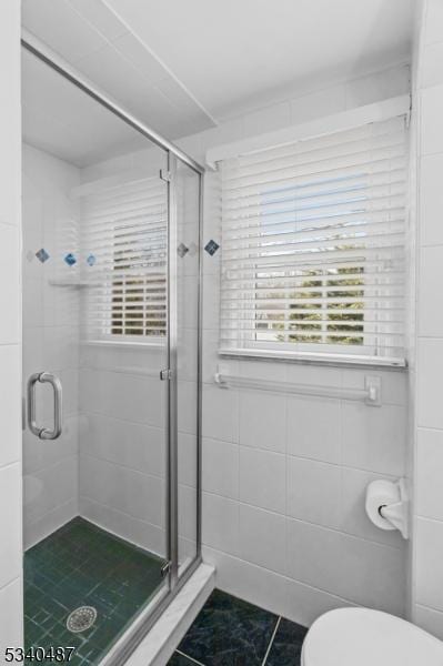 bathroom with toilet, a stall shower, and tile walls