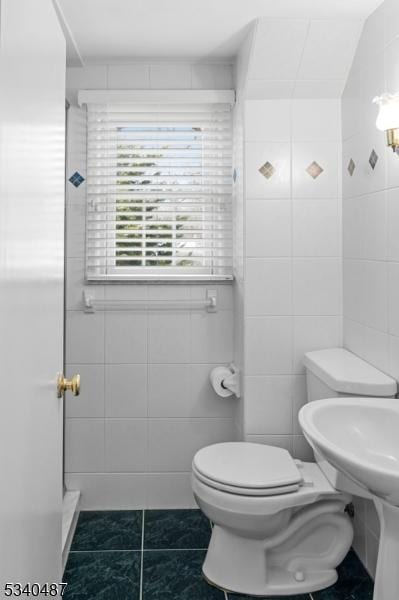 bathroom with toilet, tile patterned flooring, and tile walls