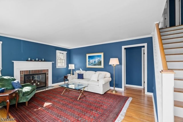 living area with ornamental molding, a brick fireplace, wood finished floors, baseboards, and stairs