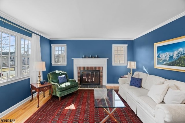 living area featuring a brick fireplace, baseboards, crown molding, and wood finished floors