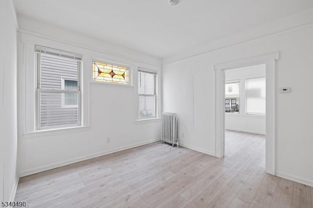 empty room with a healthy amount of sunlight, light wood-style floors, radiator heating unit, and baseboards