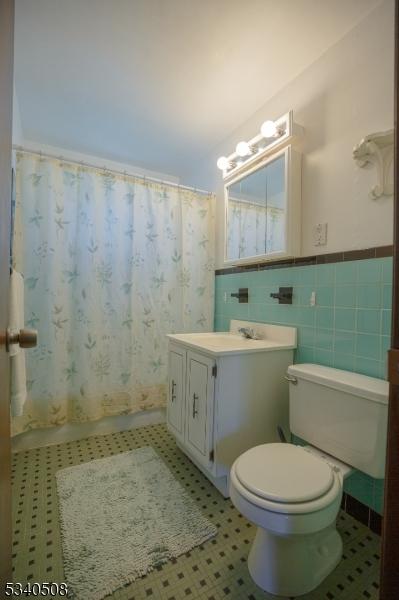 bathroom featuring tile patterned flooring, toilet, vanity, tile walls, and wainscoting