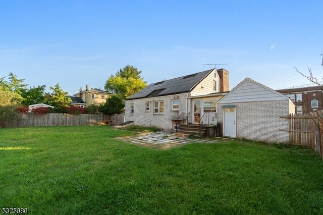 rear view of property featuring brick siding, a yard, a chimney, roof mounted solar panels, and a fenced backyard