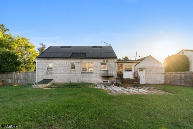 rear view of property featuring brick siding, a fenced backyard, roof mounted solar panels, and a yard