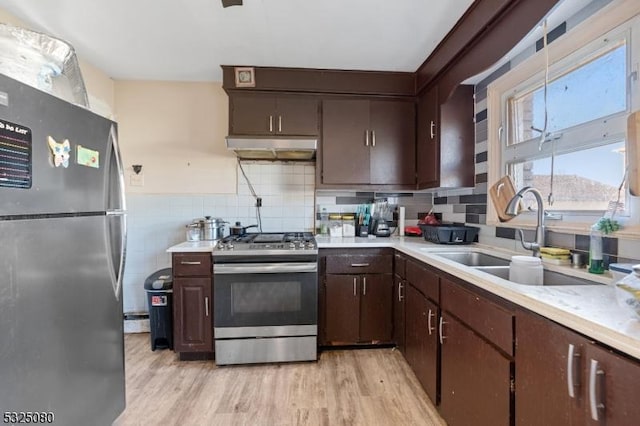 kitchen with stainless steel appliances, light countertops, a sink, dark brown cabinets, and light wood-type flooring
