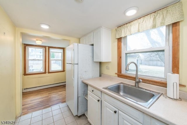 kitchen featuring a sink, baseboard heating, white cabinets, and light tile patterned flooring