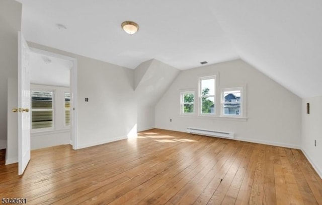 additional living space featuring visible vents, light wood-style flooring, a baseboard heating unit, vaulted ceiling, and baseboards