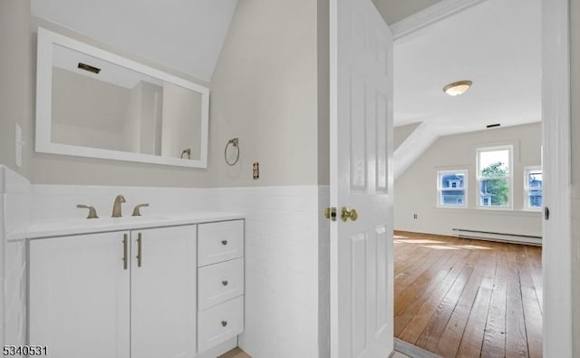 bathroom featuring wainscoting, wood-type flooring, vaulted ceiling, baseboard heating, and vanity