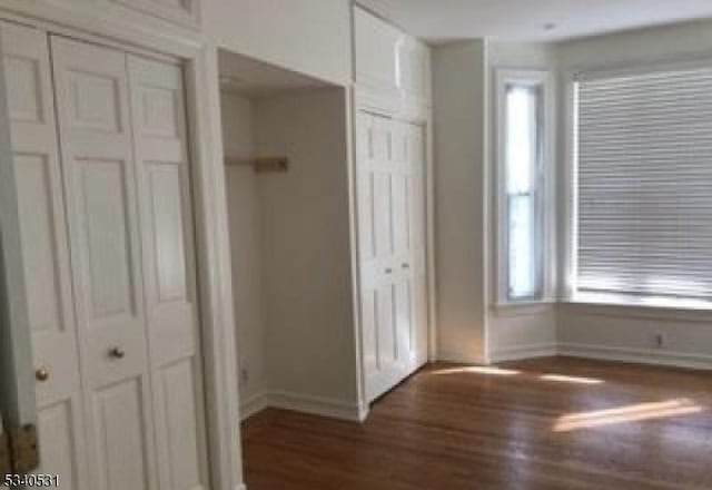 unfurnished bedroom featuring baseboards, wood finished floors, and multiple closets