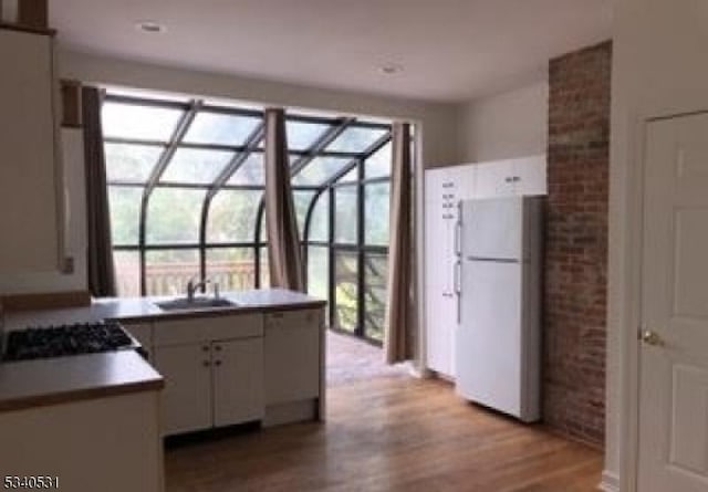 kitchen with a sink, a sunroom, white cabinets, freestanding refrigerator, and light wood finished floors