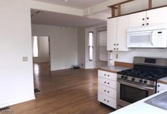 kitchen with baseboards, dark wood finished floors, white microwave, gas range, and white cabinetry