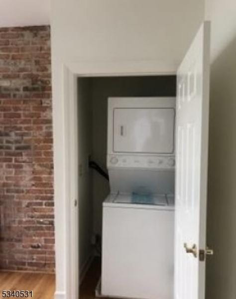 laundry area with laundry area, wood finished floors, brick wall, and stacked washer / drying machine