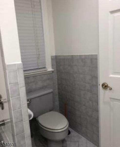 bathroom featuring toilet, a wainscoted wall, and tile walls