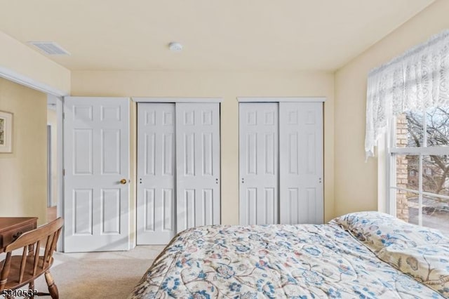 bedroom with carpet, two closets, and visible vents