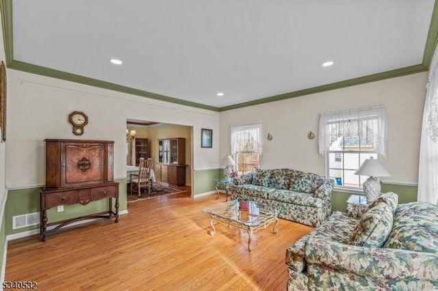 living area with baseboards, crown molding, visible vents, and wood finished floors