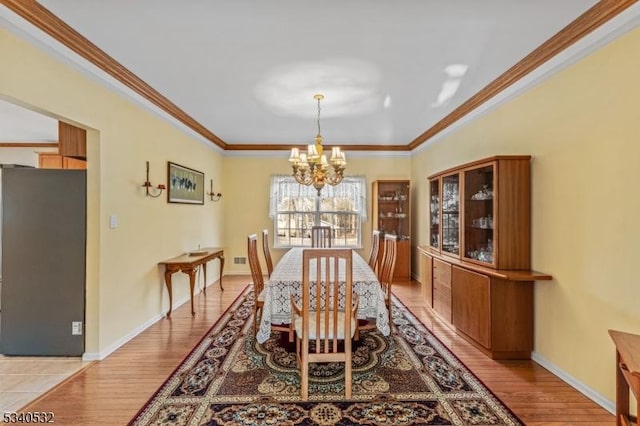 dining area featuring ornamental molding, light wood finished floors, baseboards, and a notable chandelier