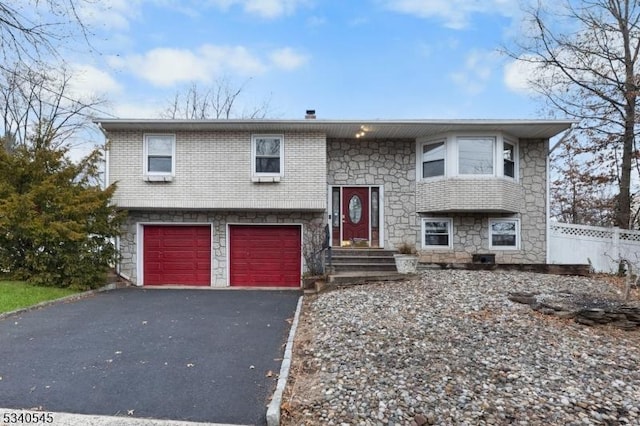 split foyer home featuring a garage, brick siding, driveway, and fence