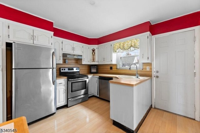 kitchen with under cabinet range hood, a sink, white cabinetry, light wood-style floors, and appliances with stainless steel finishes