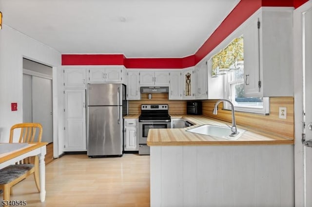 kitchen with under cabinet range hood, stainless steel appliances, a sink, light wood-style floors, and light countertops