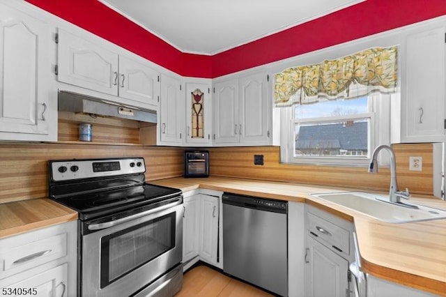 kitchen with under cabinet range hood, stainless steel appliances, a sink, white cabinetry, and wooden counters