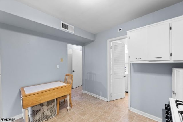 kitchen with visible vents, range, baseboards, and white cabinetry