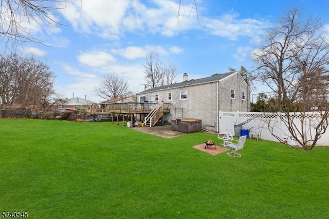 rear view of property with a deck, an outdoor fire pit, fence, a lawn, and a hot tub