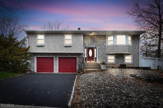 split foyer home with driveway, a garage, fence, and brick siding