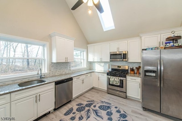 kitchen featuring tasteful backsplash, white cabinets, light wood-style flooring, stainless steel appliances, and a sink