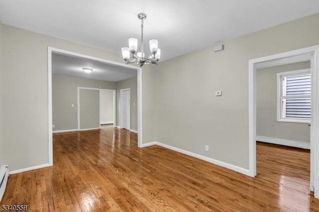 unfurnished room with a notable chandelier, baseboards, and wood finished floors