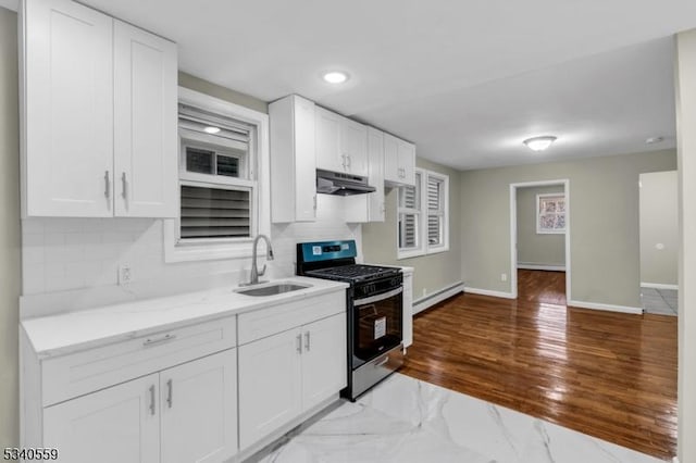 kitchen featuring white cabinets, stainless steel gas range, under cabinet range hood, a baseboard heating unit, and a sink