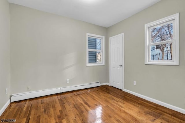 unfurnished room featuring baseboards, baseboard heating, and wood finished floors