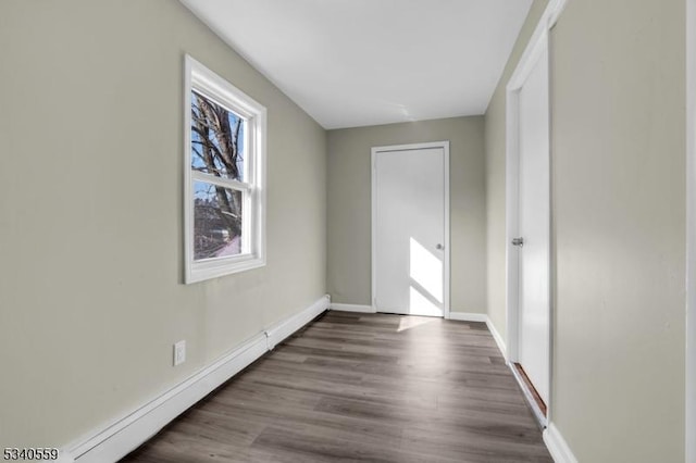 unfurnished room featuring a baseboard radiator, baseboards, and wood finished floors