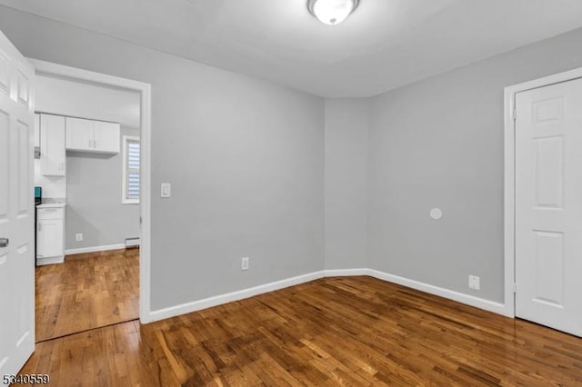 empty room featuring a baseboard heating unit, wood finished floors, and baseboards