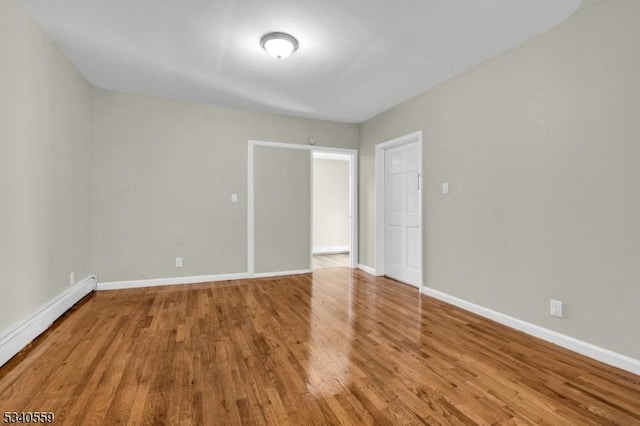 spare room featuring a baseboard radiator, wood finished floors, and baseboards