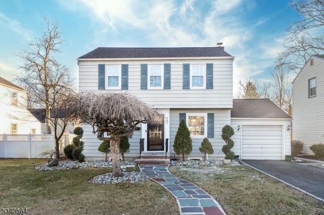 colonial-style house featuring a front lawn, driveway, an attached garage, and fence