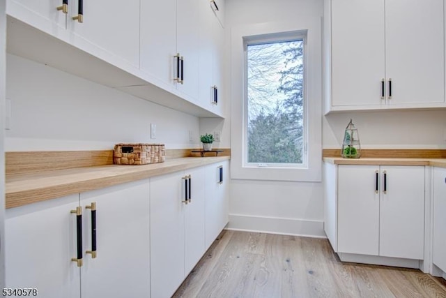 kitchen featuring baseboards, light countertops, light wood finished floors, and white cabinetry