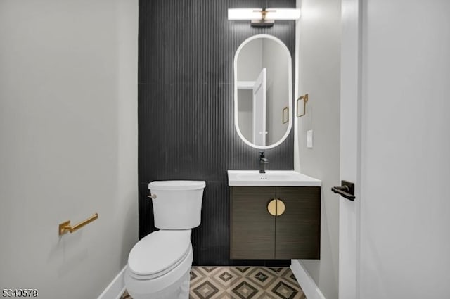 half bathroom with vanity, toilet, and baseboards