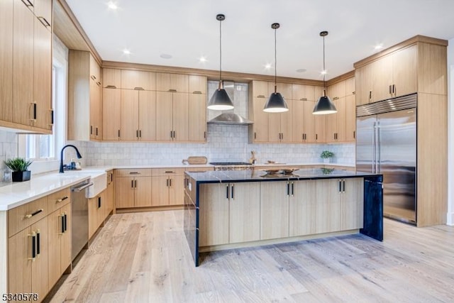 kitchen featuring stainless steel appliances, light brown cabinets, a sink, wall chimney range hood, and a kitchen island