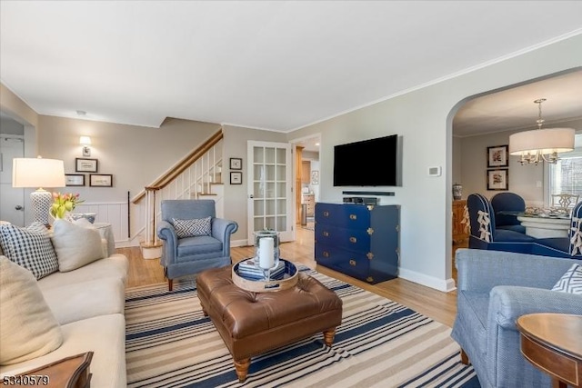 living area featuring arched walkways, stairway, an inviting chandelier, ornamental molding, and wood finished floors