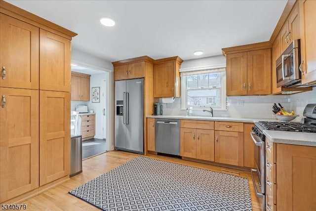 kitchen featuring decorative backsplash, stainless steel appliances, light countertops, light wood-style floors, and a sink