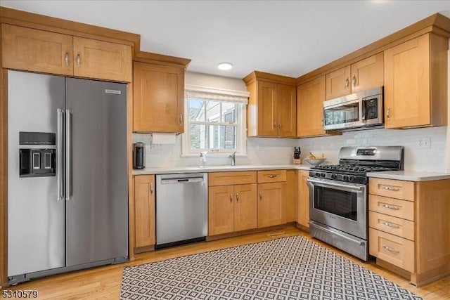 kitchen with decorative backsplash, light wood-style flooring, appliances with stainless steel finishes, light countertops, and a sink